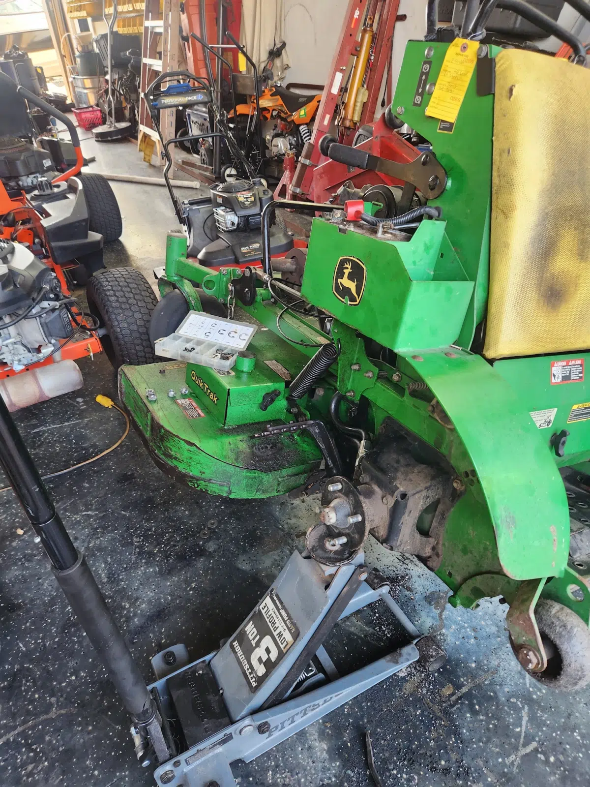 John Deere stand-on mower raised on a floor jack inside the shop — Tri County Small Engine Repair in Cape Coral